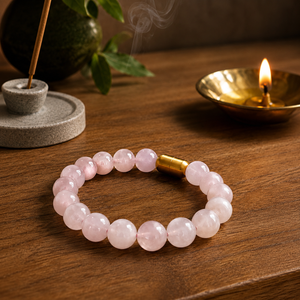 Rose quartz magsnap bracelet on a wooden table with a lit brass diya and incense behind